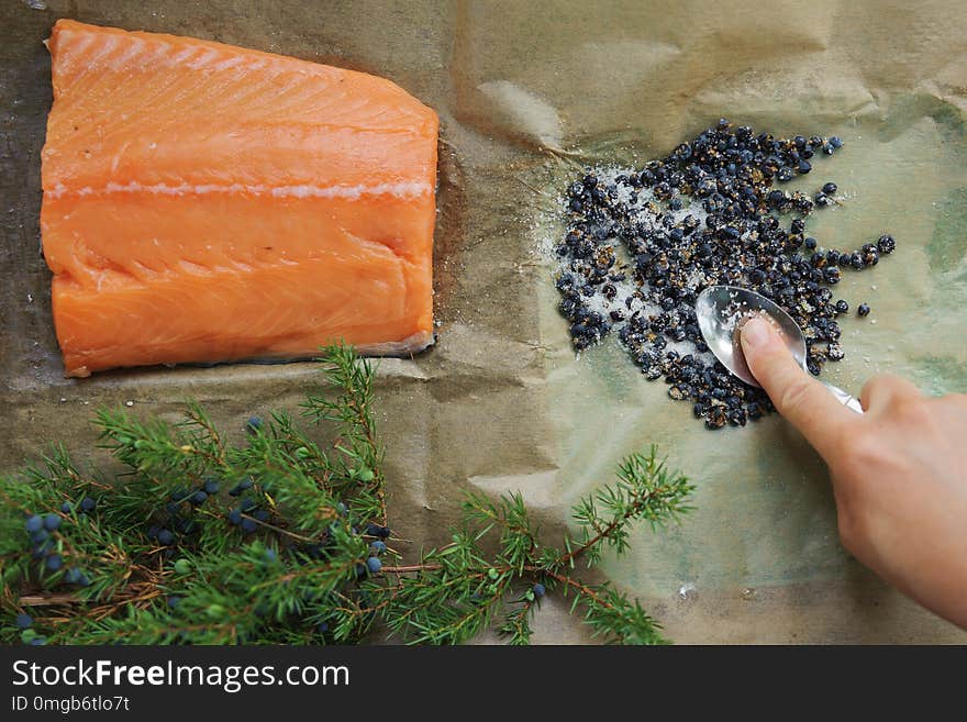 Raw salmon fillet, salt and juniper berries for cooking on brown paper in rustic style.