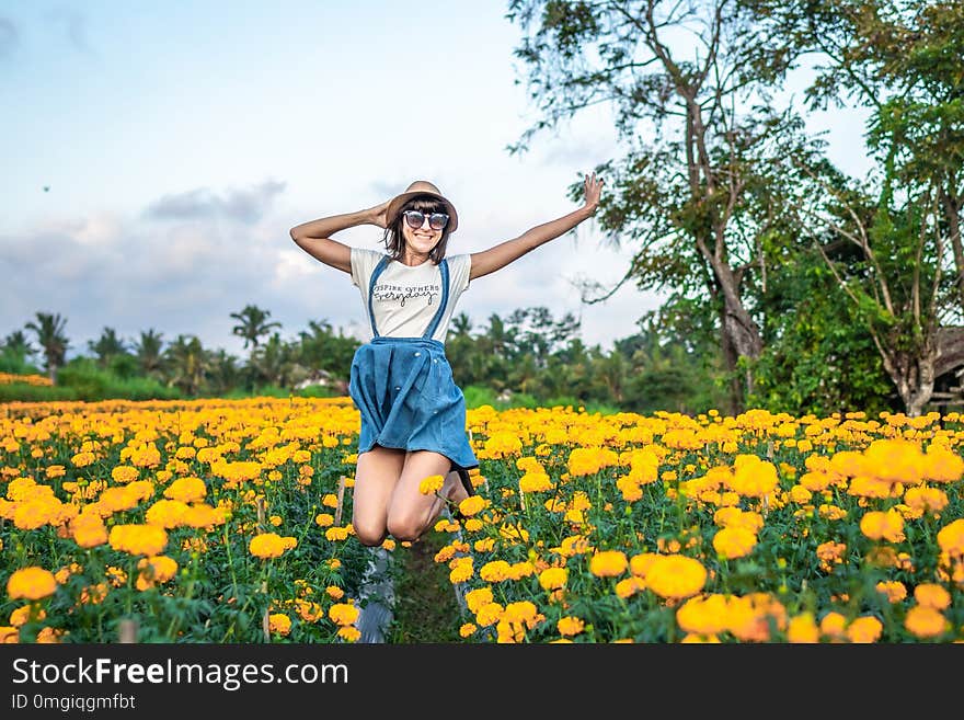 Close up portrait of happy and beautiful young woman relaxing enjoying the fresh beauty of gorgeous orange marigold flowers field in travel and holidays.