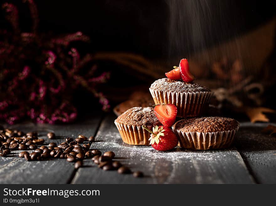 Sugar falling on muffins with strawberries laid on a jute bag with coffee beans and pink heather in the background. Sugar falling on muffins with strawberries laid on a jute bag with coffee beans and pink heather in the background.