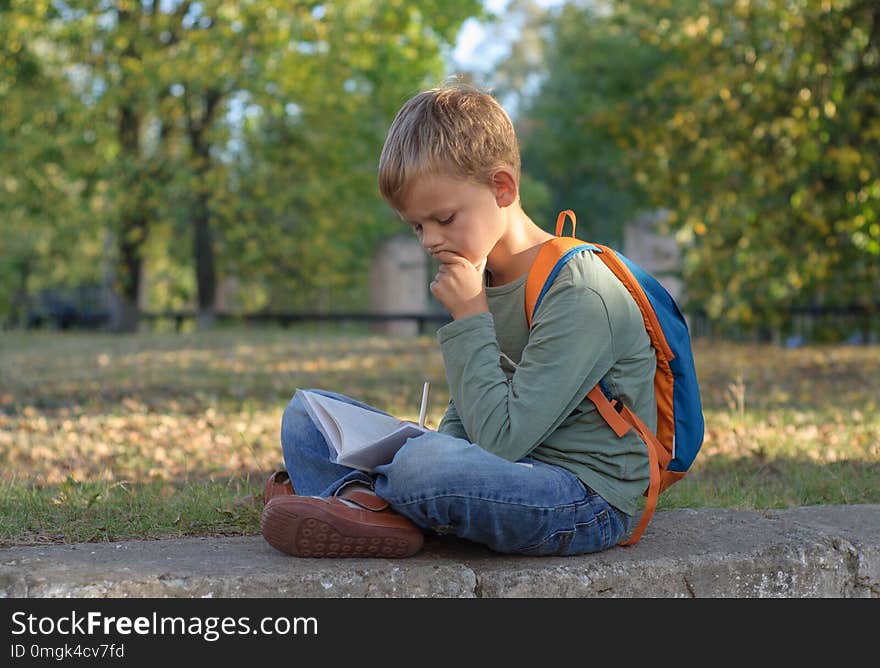 European boy student doing homework in a notebook, sitting in a beautiful autumn Park. European boy student doing homework in a notebook, sitting in a beautiful autumn Park