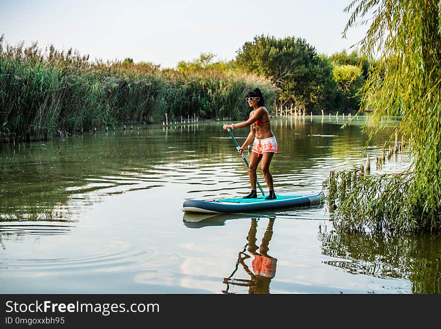 Woman stand up paddleboarding on lake. Young girl doing watersport on lake. Female tourist in swimwear during summer vacation.