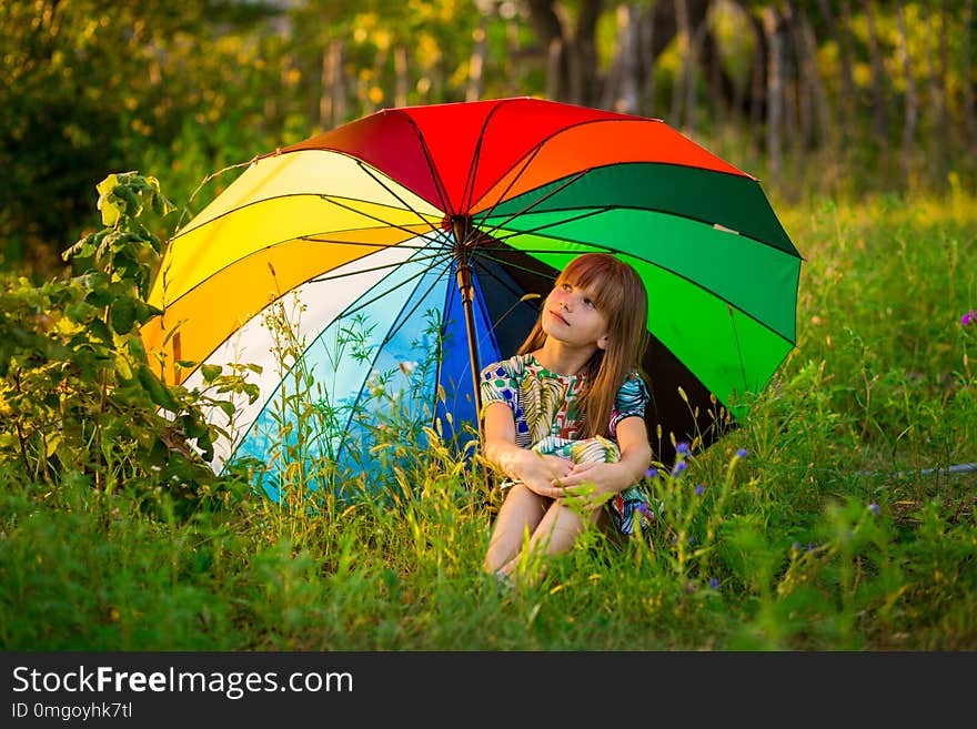 Happy child girl walk with multicolored umbrella under summer rain