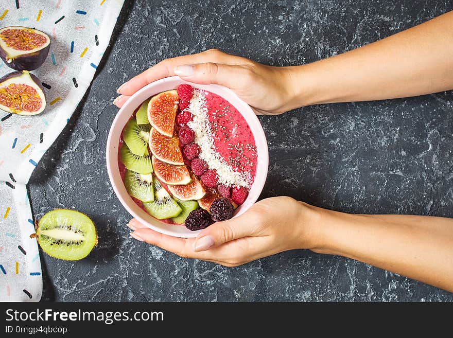 Woman hands hold raspberries smoothie bowl with figs, kiwi and coconut on concrete background