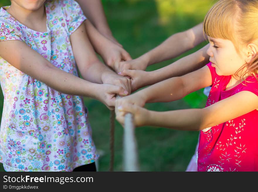 Group of happy children playing tug of war outside on grass. Kids pulling rope at park. Summer camp fun