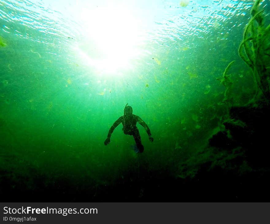 Freediver descending into a sinkhole with a high algae content, in front of a setting sun Limestone Coast, South Australia. Freediver descending into a sinkhole with a high algae content, in front of a setting sun Limestone Coast, South Australia.