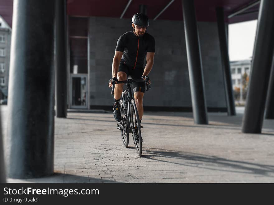 Sportsman riding bike next to modern building inside urban bridge.