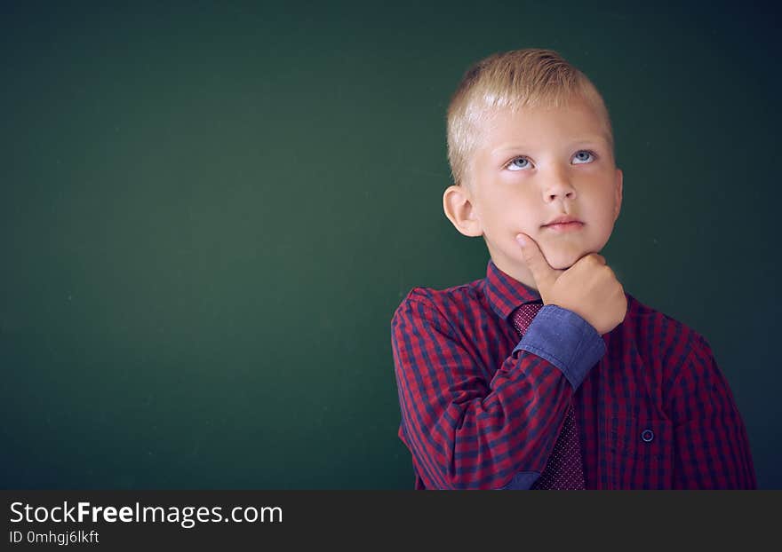 Closeup shot of schoolboy thinking with hand on chin isolated on blackboard. Portrait of pensive Caucasian litlle boy thinking about task. Copy space. Closeup shot of schoolboy thinking with hand on chin isolated on blackboard. Portrait of pensive Caucasian litlle boy thinking about task. Copy space.
