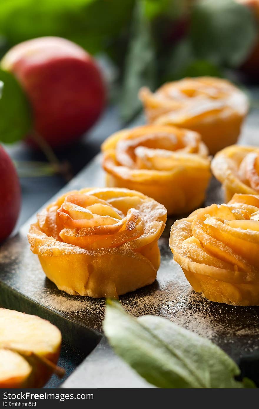 Apple Rose mini tarts with icing sugar on the stone cutting board.