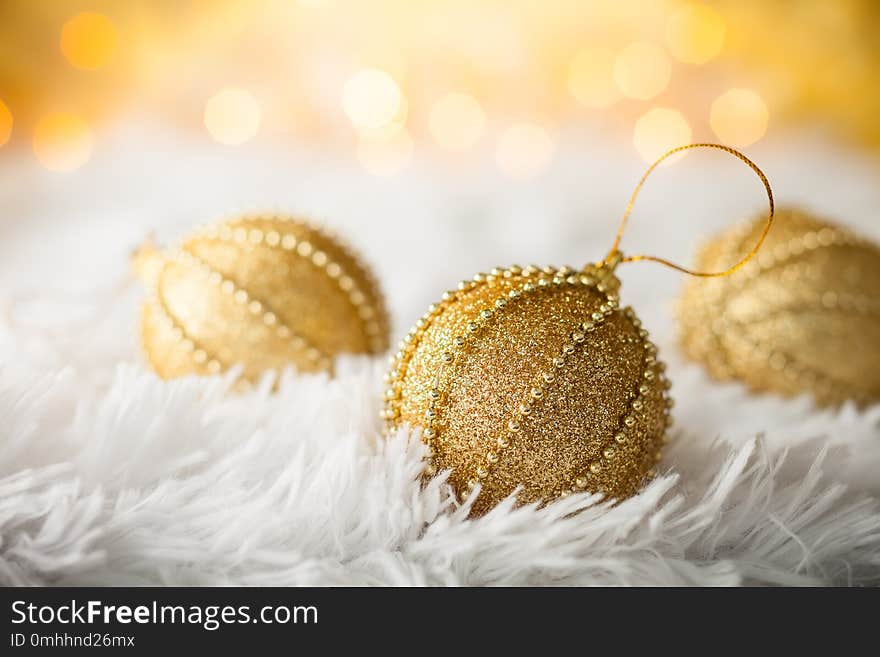 Gold Christmas baubles on white fur with gold sparkling background. Festive winter concept.