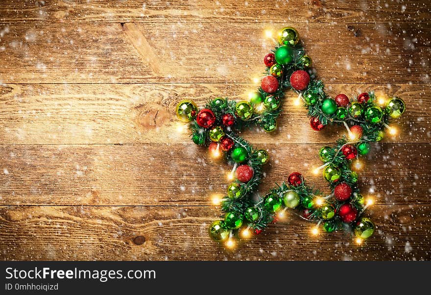 Decorative Christmas Star with colored baubles, christmas tree branches and lights on the rustic wooden board. Top view.