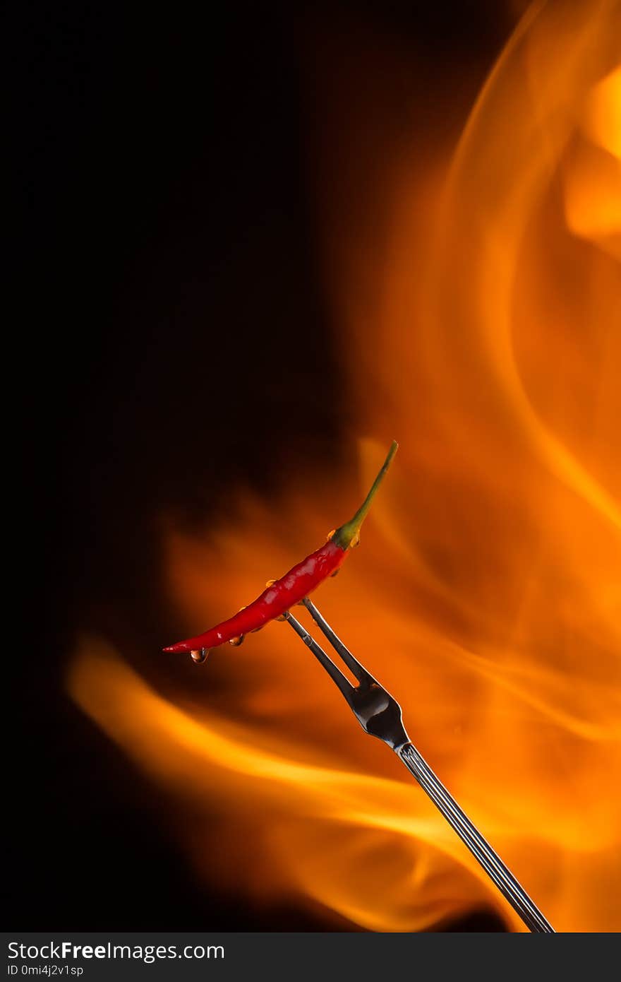 Chilli pepper on meat fork with flame behind on black background