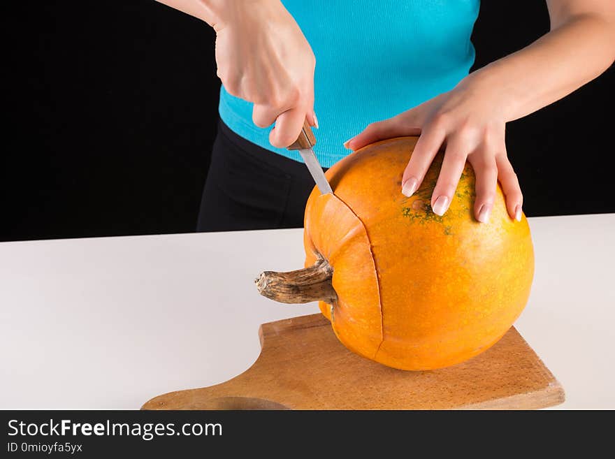 Young woman hand cuts big orange pumpkin on wooden board isolated on black background. Halloween and Thanksgiving day food concept. Close up. Young woman hand cuts big orange pumpkin on wooden board isolated on black background. Halloween and Thanksgiving day food concept. Close up