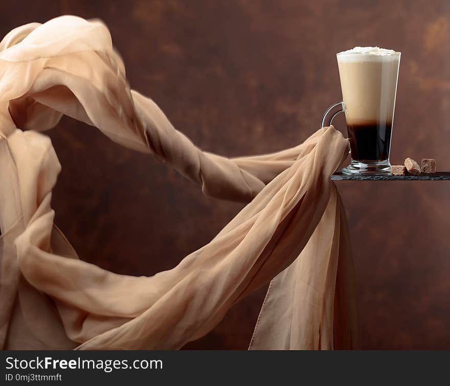 Coffee drink with cream and pieces of brown sugar on a brown background. Evolving in the wind chiffon scarf. Copy space for your text. Coffee drink with cream and pieces of brown sugar on a brown background. Evolving in the wind chiffon scarf. Copy space for your text.