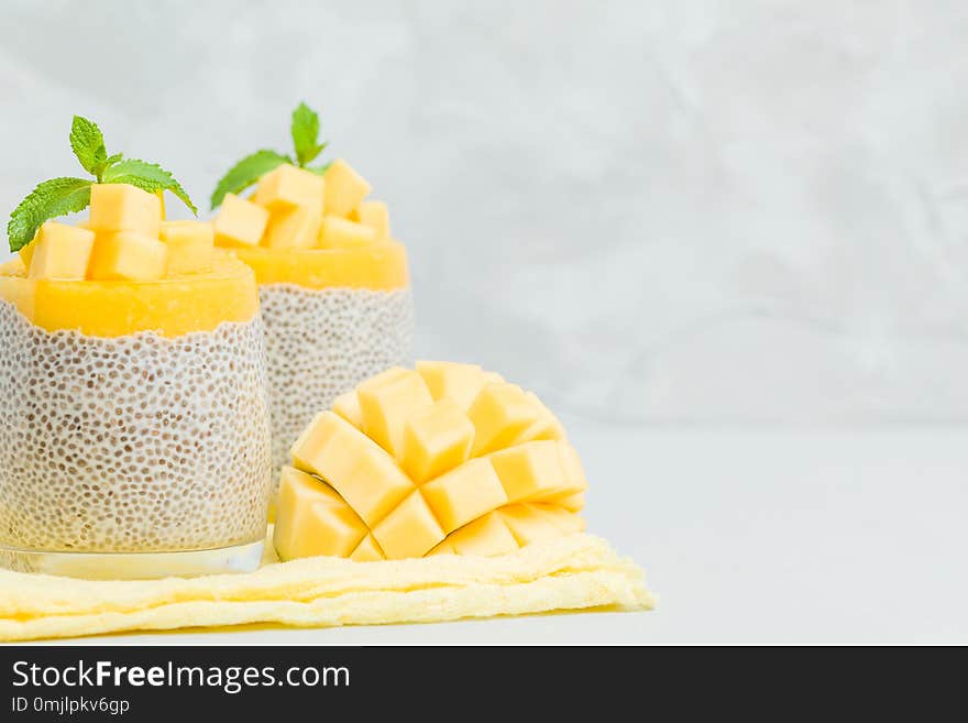 Chia seeds pudding with mango puree in beautiful glasses with green mint leaves and cut fresh ripe tropical fruit.