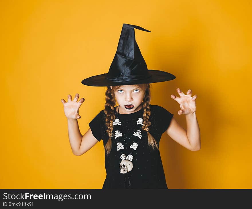 Beautiful young halloween witch on orange background with black hat