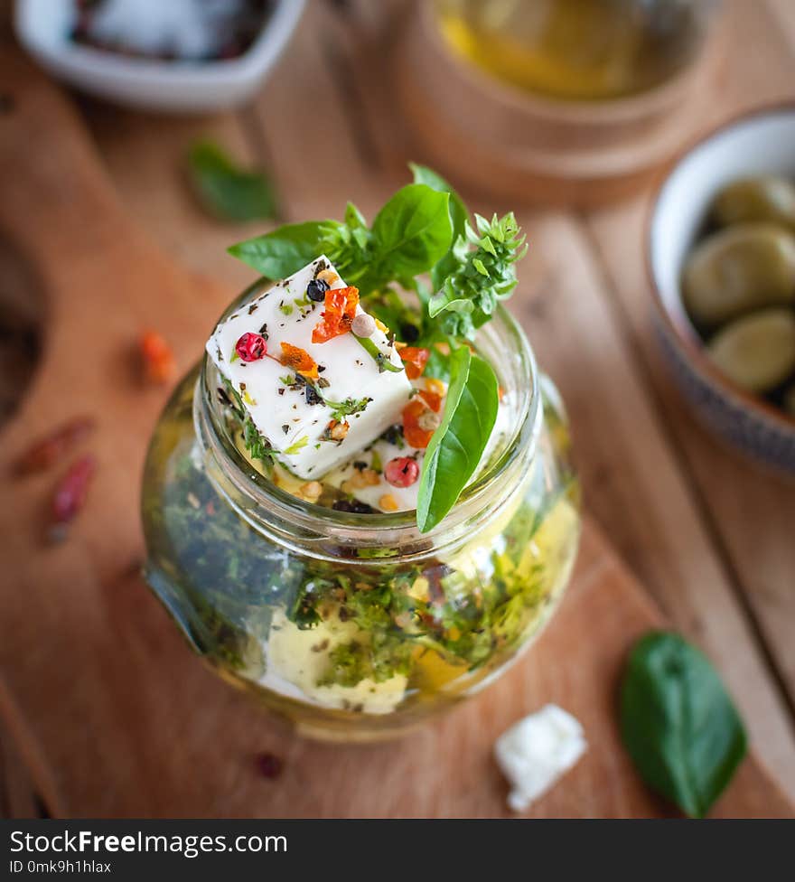 Close-up of marinated feta cheese in olive oil, herbs and red pepper flakes on wooden background.