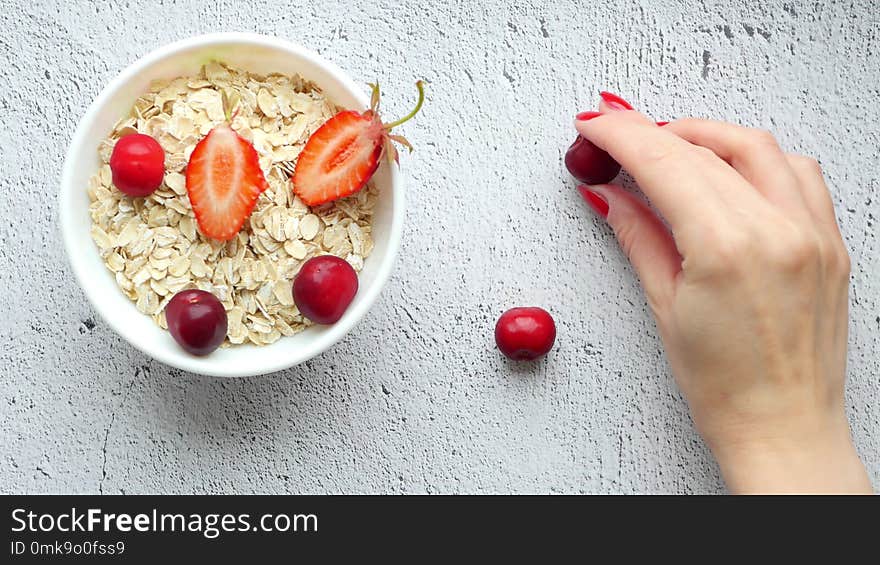 Beautiful female hands lay out on the table a composition of bright berries. Juicy red cherries on a white background. Bowl of oatmeal. Healthy breakfast. Proper nutrition. Fault on the table. 4k. Beautiful female hands lay out on the table a composition of bright berries. Juicy red cherries on a white background. Bowl of oatmeal. Healthy breakfast. Proper nutrition. Fault on the table. 4k