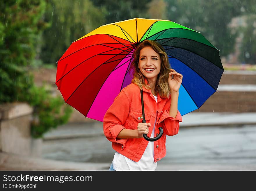 Happy young woman with bright umbrella under rain outdoors