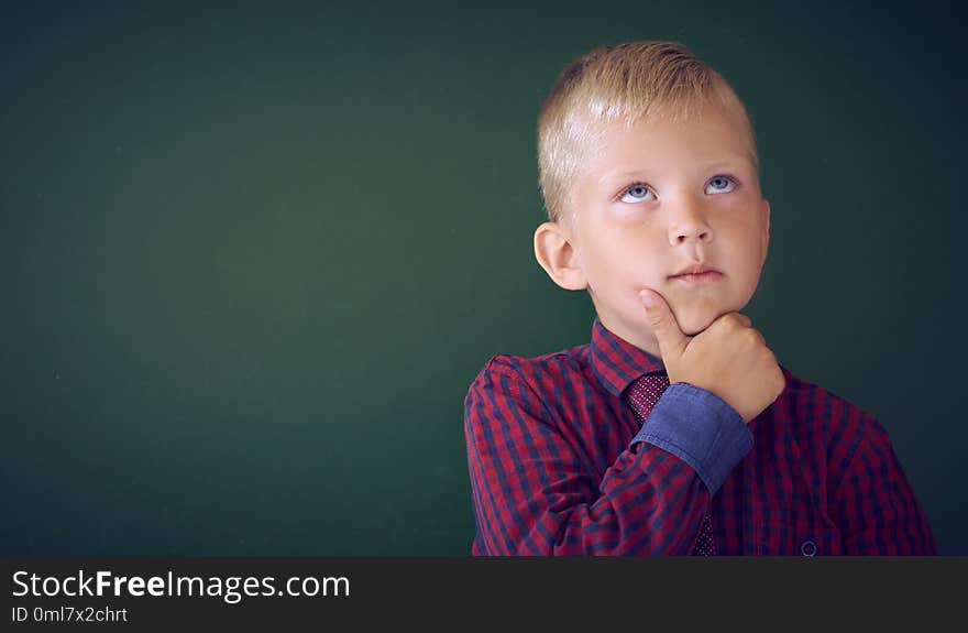 Closeup shot of schoolboy thinking with hand on chin isolated on blackboard. Portrait of pensive Caucasian litlle boy thinking about task. Copy space. Closeup shot of schoolboy thinking with hand on chin isolated on blackboard. Portrait of pensive Caucasian litlle boy thinking about task. Copy space.