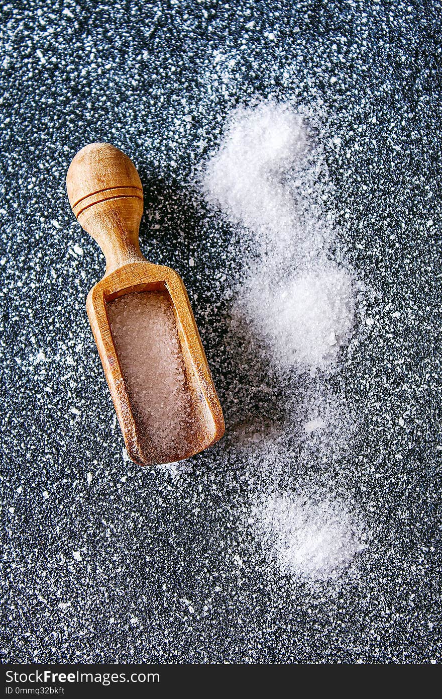 Crystals of shallow salt in a scoop, spoon on a dark gray table.