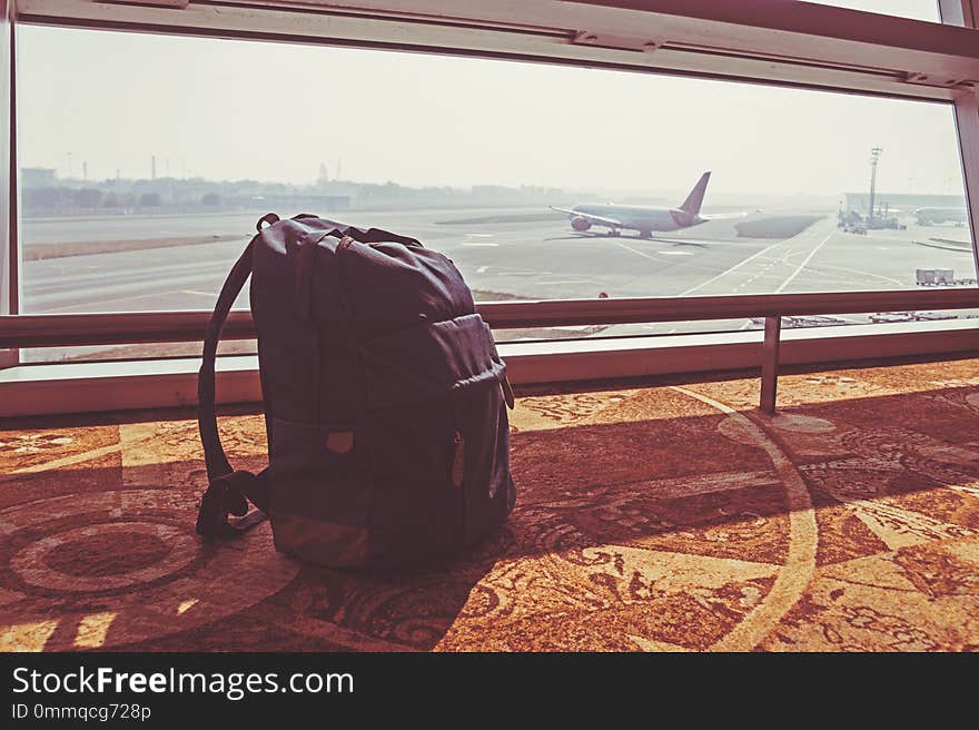 Silhouette of luggage or suitcase placed at the window at waiting terminal in international airports with the airplan taking off behide the building.