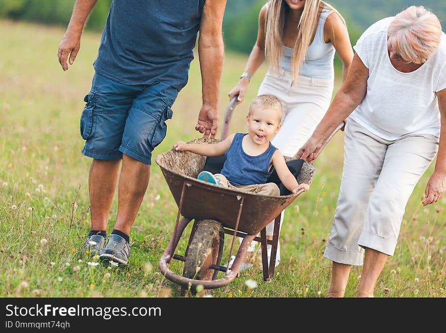 Family pushing their small child and grandchild in a wheelbarrow. Family pushing their small child and grandchild in a wheelbarrow