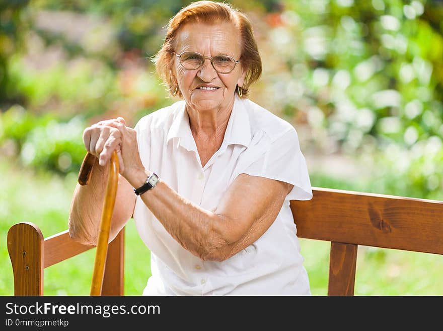 Elderly woman sitting and relaxing on a bench in park