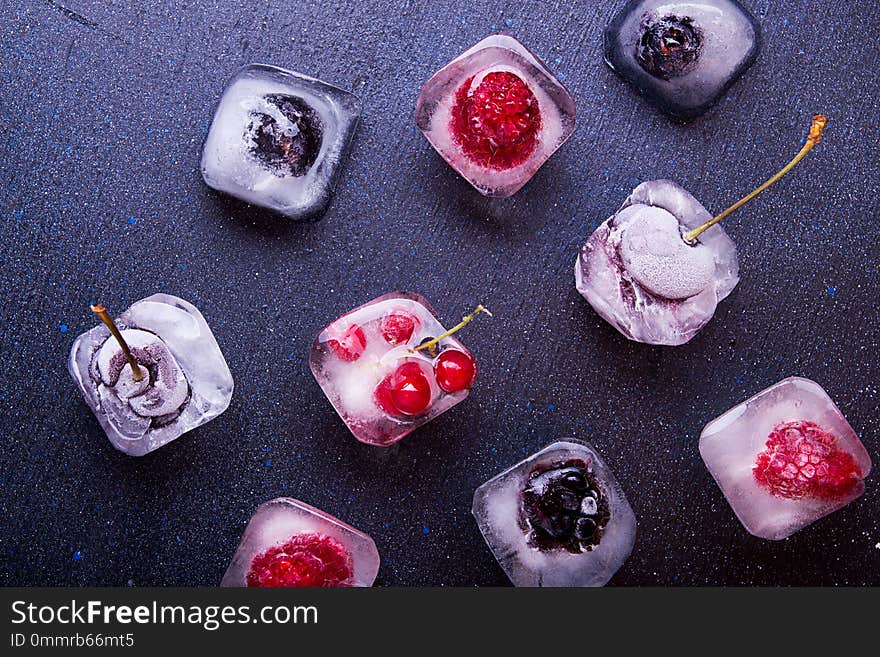 Frozen berries raspberries, blackberries, blueberries, red currant, cherry in ice cube over white fabric background. Top view.