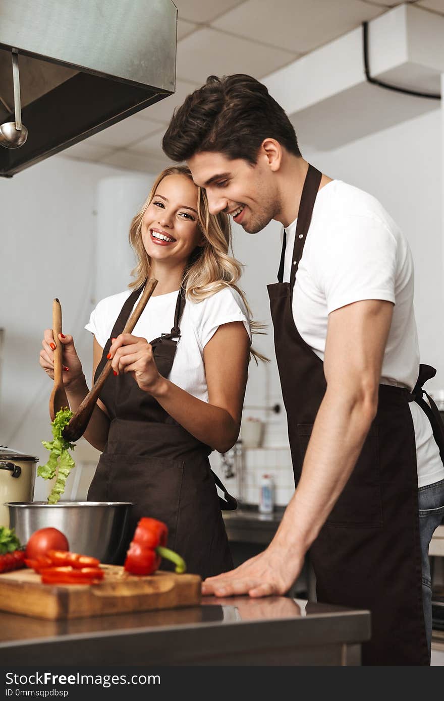 Smiling excited young friends loving couple chefs on the kitchen cooking.