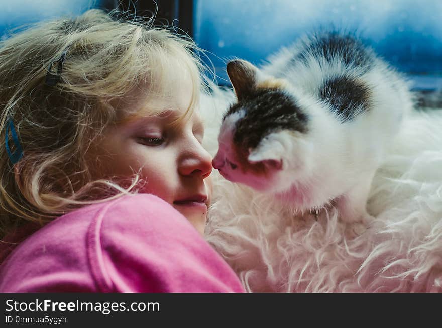 Lovely blond girl and a cat by the window looking into eyes in winter time. Lovely blond girl and a cat by the window looking into eyes in winter time