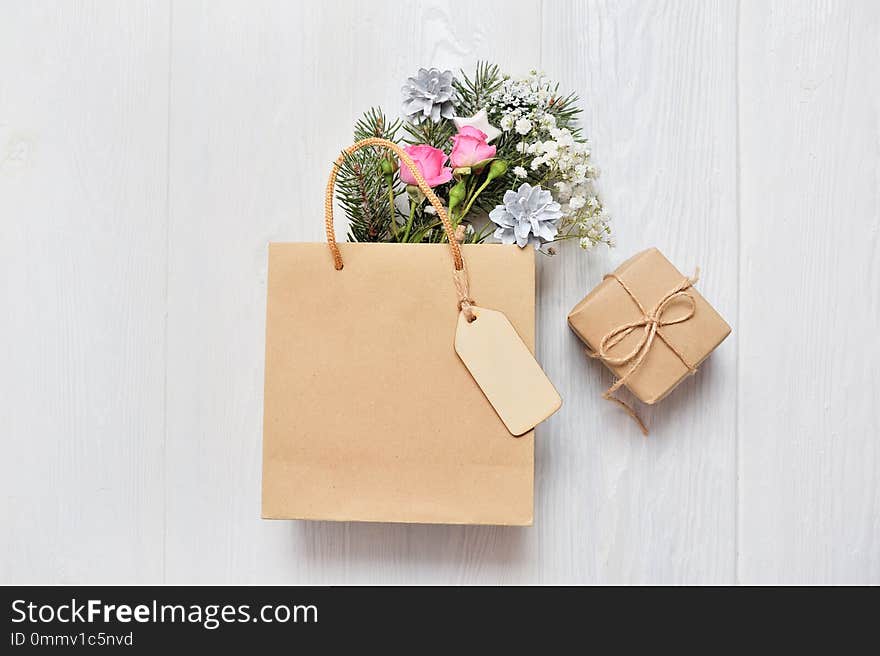 Christmas mockup shopping concept. Kraft package with wooden tag and xmas decor fir branches, pink roses, cones with place for your text.