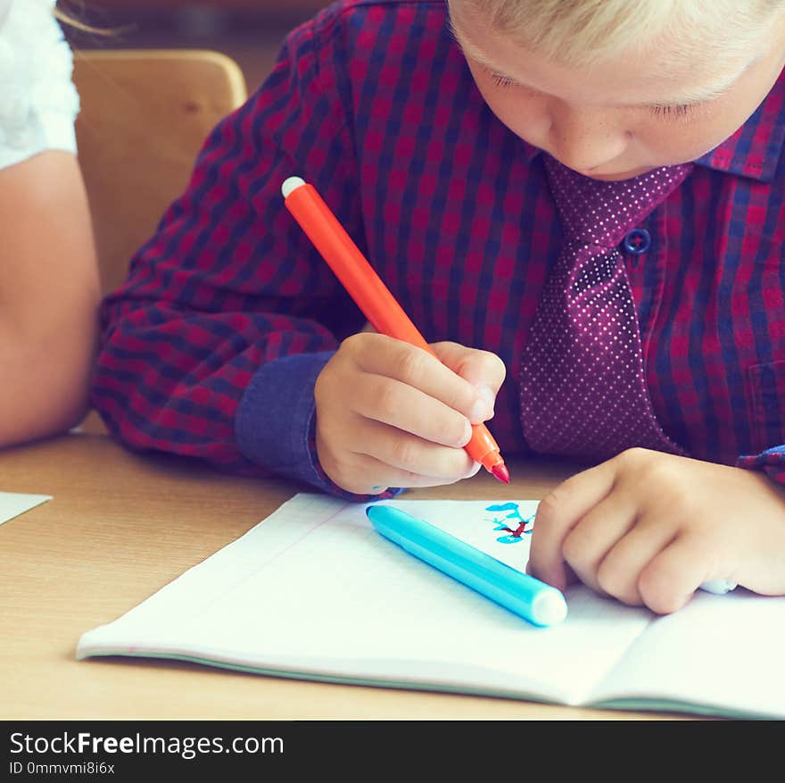 Little boy is painting a picture with felt-tip pens siting at the table. Drawing in kindergarten, school. Children`s development, art therapy for children. Little boy is painting a picture with felt-tip pens siting at the table. Drawing in kindergarten, school. Children`s development, art therapy for children.