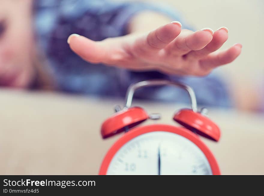 Young girl lies on the couch and stretches her hand to the red alarm clock to turn it off. Late wake up.