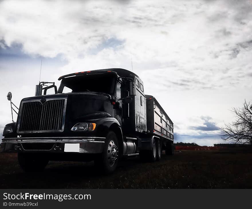 An imposing desaturated view of a semi truck and grain trailer under a cloudy autumn sky. An imposing desaturated view of a semi truck and grain trailer under a cloudy autumn sky