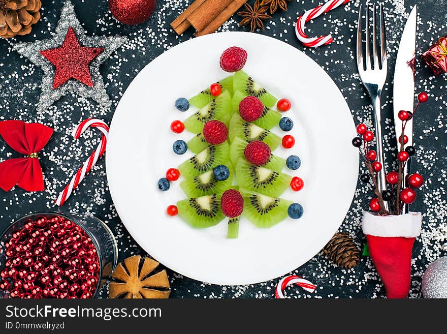 Kiwi christmas tree with raspberry, blueberry and cowberry on table with decoration. Christmas and New Year food background. top view