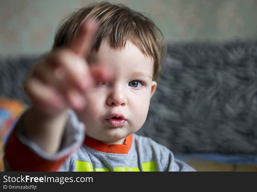 Boy child or small kid with serious face pointing with his pointer finger. Little boy points direction by forefinger