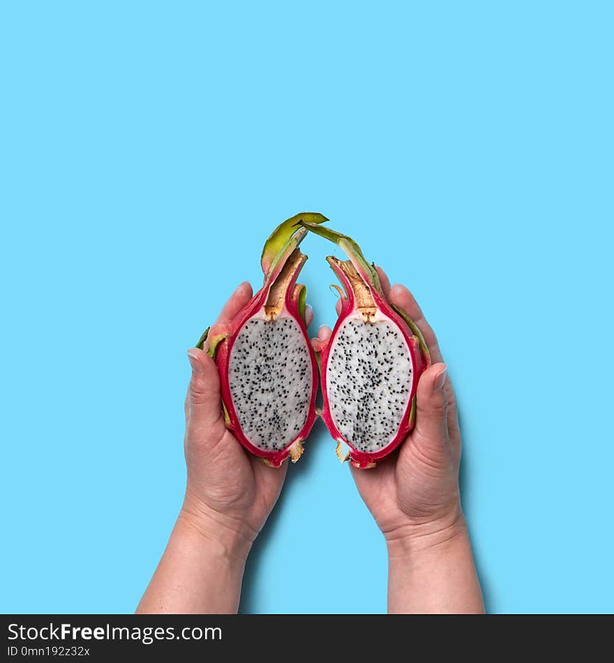 Halves of an organic exotic fruit pitahaya hold the woman`s hands on a blue background with space for text. Flat lay. Halves of an organic exotic fruit pitahaya hold the woman`s hands on a blue background with space for text. Flat lay