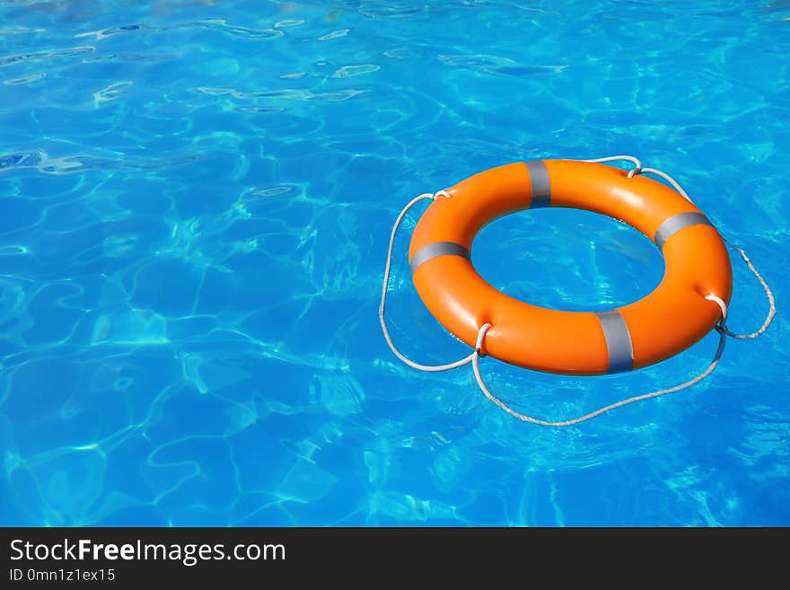 Lifebuoy floating in swimming pool on sunny day. Space for text