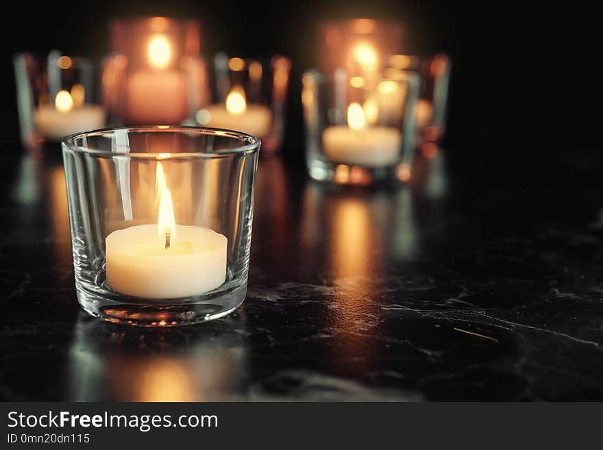 Burning candle on table in darkness, space for text