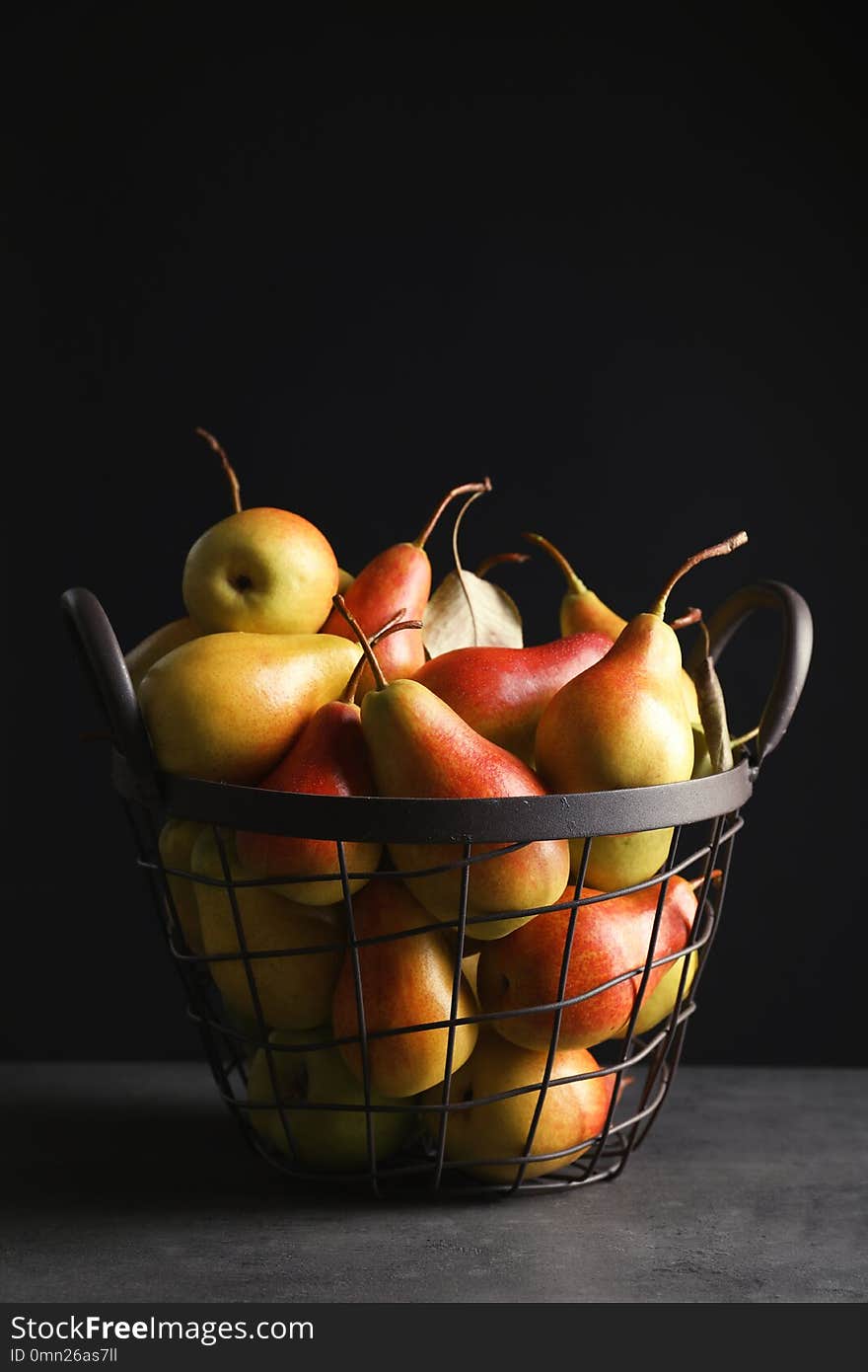 Basket with ripe pears on table against black background. Space for text