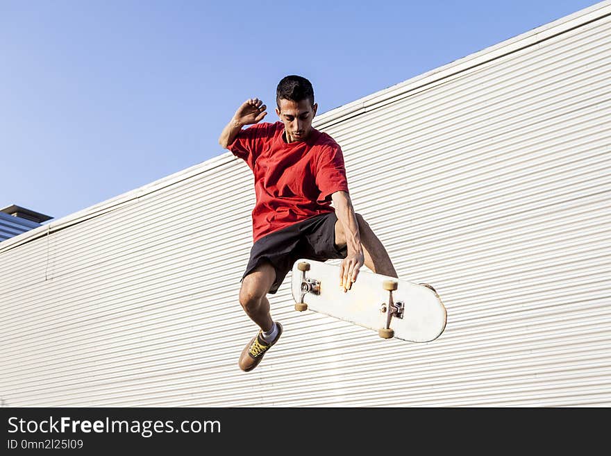 Young skateboarder jumps up with his board in front of a metal background on the roofs of an abandoned building