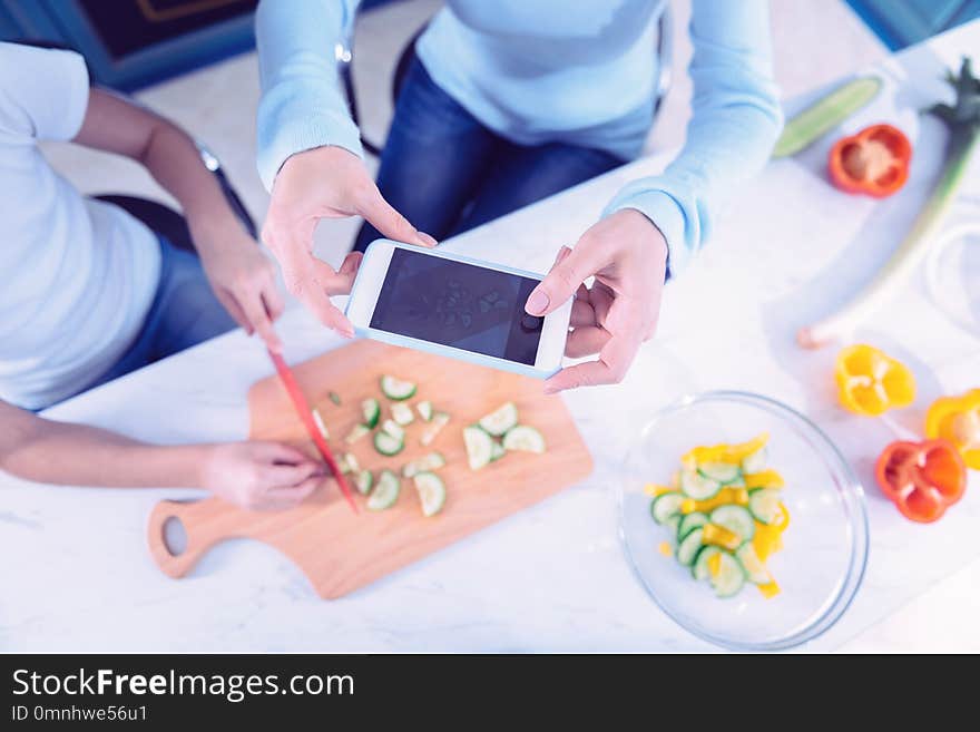 Photos of cucumbers. Active young women holding her modern smartphone and carefully taking photos of cucumbers on the table. Photos of cucumbers. Active young women holding her modern smartphone and carefully taking photos of cucumbers on the table