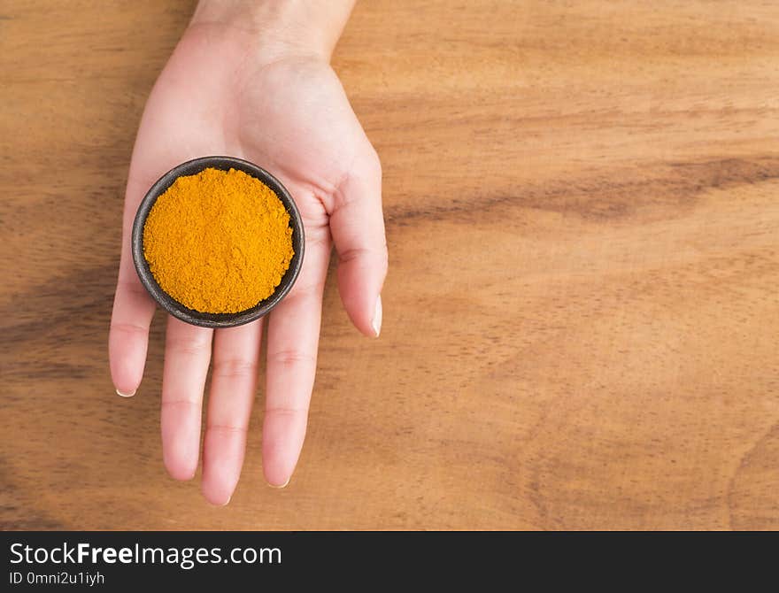 Turmeric powder in bowl between hands - Curcuma longa. Top view