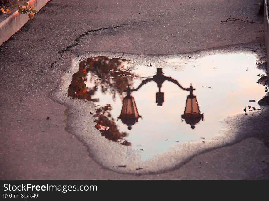 Interesting reflection of a lantern in a puddle in a hole on the afalt with a crack in the light of the setting sun. Mirror image after the rain in the sunset evening.