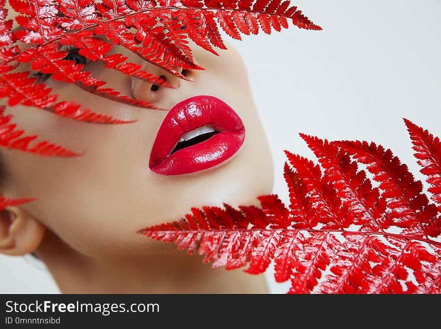 A woman with Sensual red lips and a fern. Woman`s mouth with red Lips. woman Red Lips on a Gray background. Female portrait with bright makeup. Lip gloss