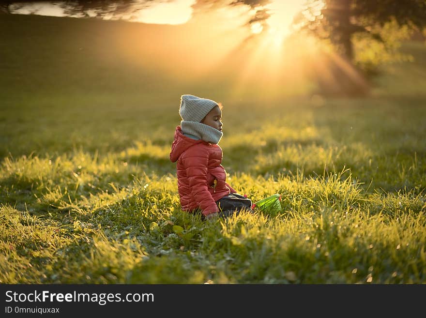 A child in the rays of a warm sun sitting on the grass.