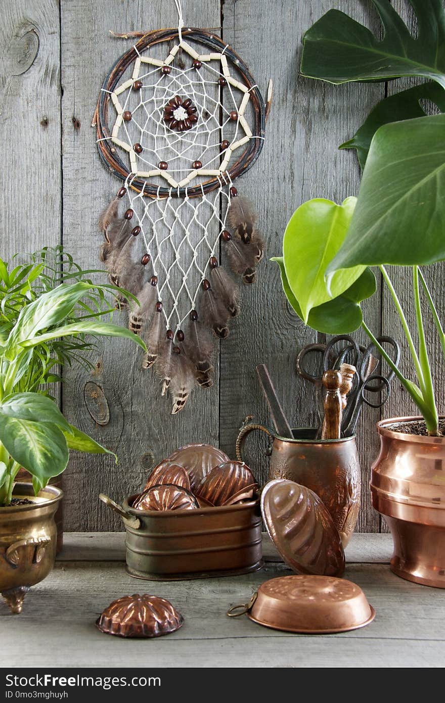 Dream catcher and vintage copper molds in interior on wooden gray background. Green plants and copy space for text. Dream catcher and vintage copper molds in interior on wooden gray background. Green plants and copy space for text.