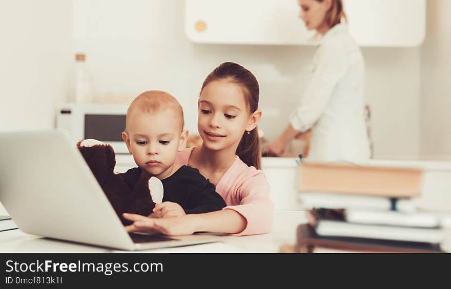 Young Girl Plays With Baby Brother On Kitchen. Happy Childhood Concept. Active Kids. Mom`s Cooking Background. Family Holiday Leisure. Writing On The Laptop Keyboard. Parent`s Duty.