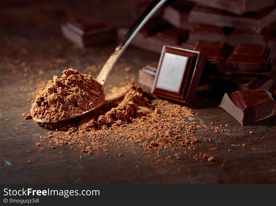 Broken chocolate pieces and cocoa powder in small spoon on a wooden background. Broken chocolate pieces and cocoa powder in small spoon on a wooden background.