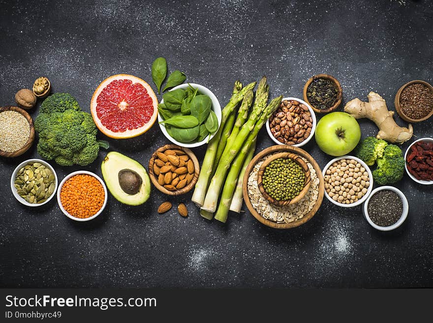 Superfoods on black stone background. Organic food and healthy vegan food. Legumes, nuts, seeds, fruit and vegetables. Top view.